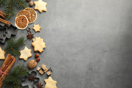 Christmas food. Cookies in shape of stars, spices, brown sugar, cutters and fir tree branches on gray table, flat lay. Space for textの写真素材