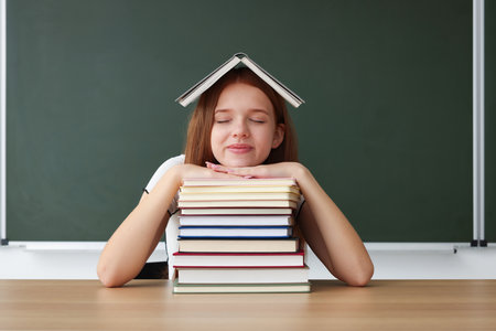 Back to school. Student with books at wooden desk against chalkboard indoorsの写真素材