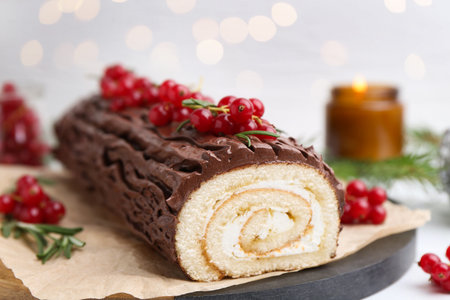 Delicious Yule log (traditional Christmas cake) with redcurrant on table against blurred lights, closeup. Bokeh effectの写真素材