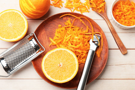 Orange zest, fresh fruits, zester tool and grater on light wooden table, flat lay