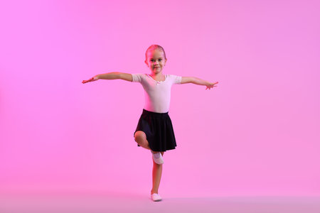 Little girl doing gymnastic exercise on violet background in color lightの写真素材