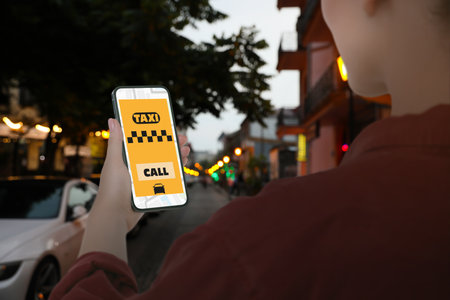 Woman using app on mobile phone to call taxi on city street, closeupの写真素材