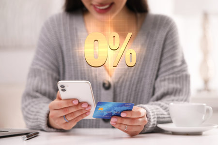 Woman with credit card using smartphone at table, closeup. 0 percent sign for zero commission