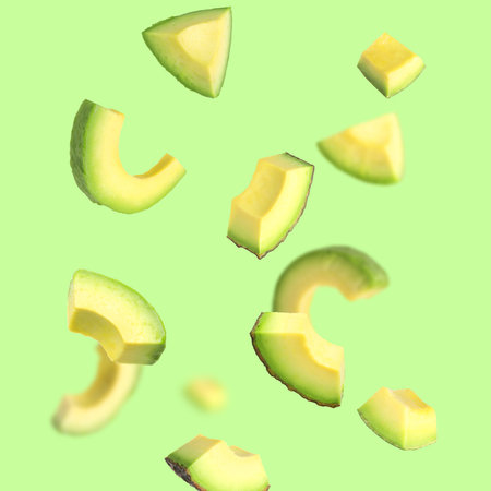 Fresh avocado slices falling on light green backgroundの写真素材