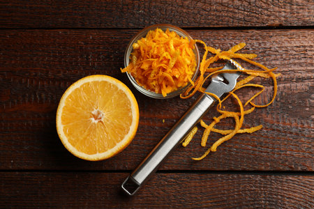 Orange zest, fresh fruit and zester tool on wooden table, flat lay