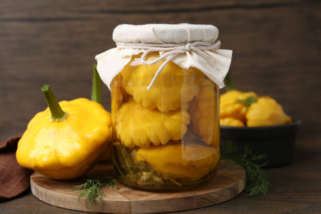 Pickled pattypan squashes in glass jar, fresh vegetables and dill on wooden table, closeupの写真素材
