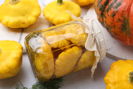 Pickled pattypan squashes in jar and fresh vegetables on light table, closeupの写真素材