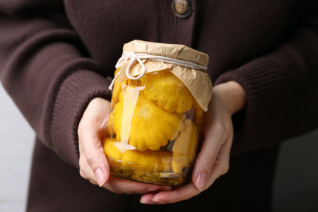 Woman with jar of pickled pattypan squashes against light gray background, closeupの写真素材