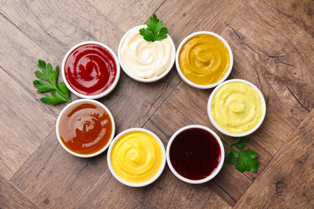 Frame made of different tasty sauces in bowls and parsley on wooden table, flat lay. Space for textの写真素材