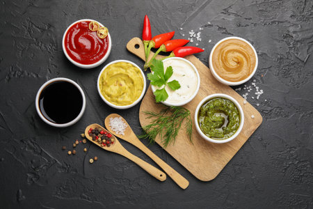 Different sauces, spices and herbs on black table, flat layの写真素材