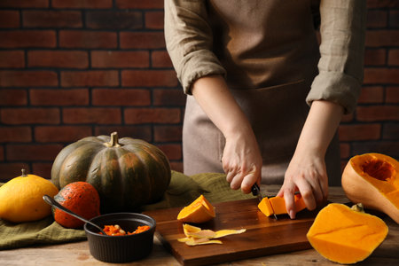 Woman cutting pumpkin at wooden table against brick wall, closeupの写真素材