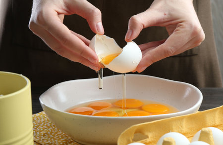 Woman breaking egg at table indoors, closeup