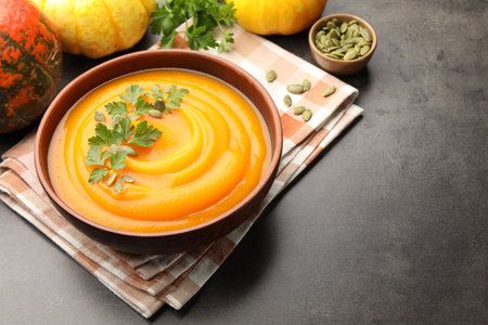 Tasty pumpkin cream soup with parsley and seeds in bowl on gray textured table, closeup. Space for textの写真素材