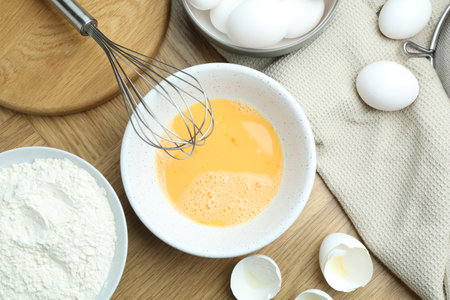 Beaten eggs in bowl, flour on wooden table, flat layの写真素材