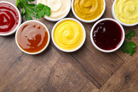 Different tasty sauces in bowls and parsley on wooden table, flat lay. Space for textの写真素材