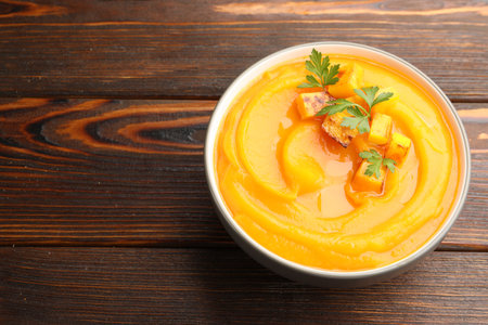 Delicious pumpkin cream soup with parsley served on wooden table, closeup. Space for textの写真素材