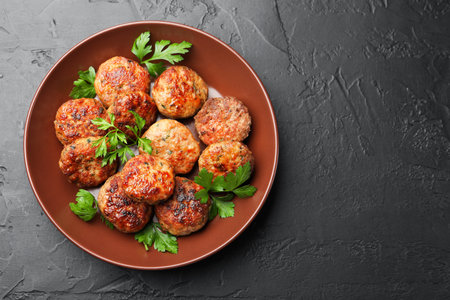 Delicious patties with parsley in bowl on dark textured table, top view. Space for textの写真素材