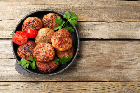 Delicious patties with parsley and tomatoes in pan on wooden table, top view. Space for textの写真素材