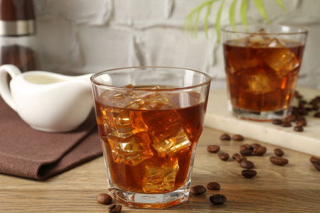 Tasty coffee with ice in glasses and beans on wooden table against light textured background,...