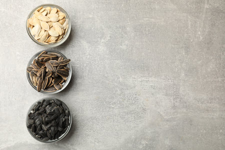 Sunflower and pumpkin seeds in bowls on gray table, flat lay. Space for textの写真素材