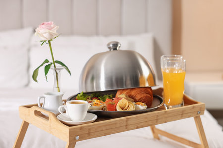Tray with delicious breakfast and rose on bed in hotel room, closeupの写真素材