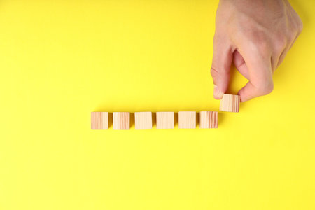 Man with wooden cubes on yellow background, top viewの写真素材