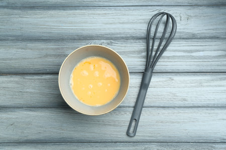 Beaten eggs in bowl on wooden table, flat layの写真素材