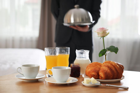 Waiter serving breakfast on wooden table in hotel room, closeupの写真素材