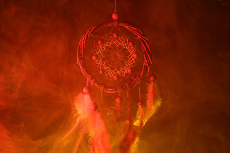 Beautiful dream catcher and smoke in color light on dark background