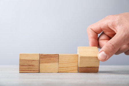 Man with wooden cubes on light background, closeup. Space for textの写真素材