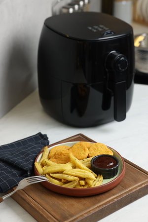 Cooked French fries, chicken nuggets, sauce and air fryer on white marble countertop, closeupの写真素材