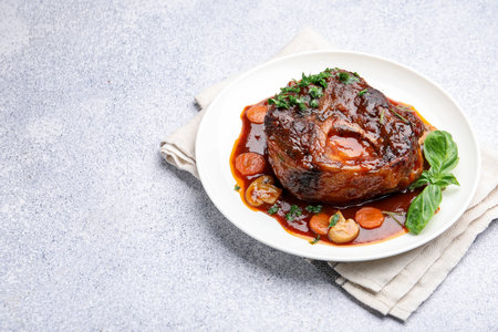 Tasty beef ossobuco with carrots, mushrooms and herbs on gray textured table, closeup. Space for textの写真素材