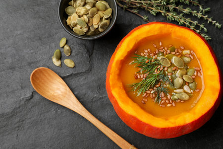Tasty pumpkin cream soup with seeds, dill and thyme on dark textured table, flat layの写真素材