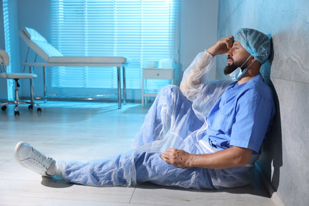 Tired doctor sitting on floor near wall in clinic during night shiftの写真素材
