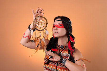 Shaman woman with face painting and dreamcatcher on pale orange gradient backgroundの写真素材