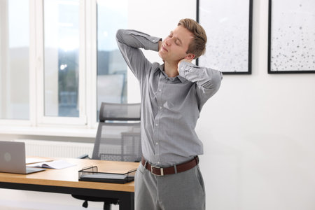 Young businessman doing stretching exercise in officeの写真素材