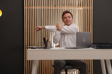 Young businessman stretching his arm at table in officeの写真素材