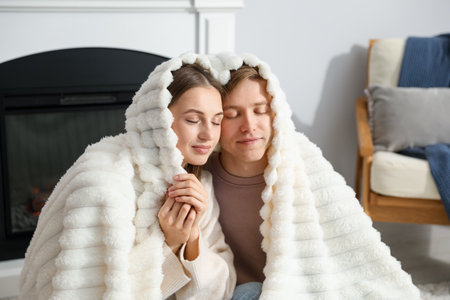 Lovely couple wrapped in blanket near fireplace indoorsの写真素材