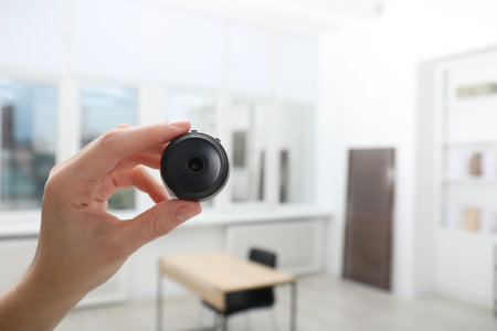 Woman with hidden camera on blurred background, closeup. Space for text