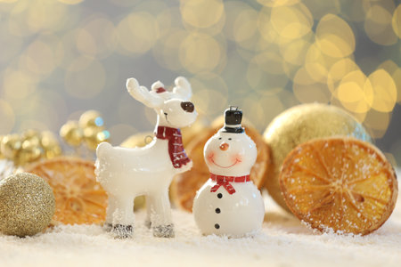 Cute decorative snowman, reindeer, dried orange slices and golden baubles on artificial snow against blurred lights, closeupの写真素材