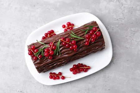 Delicious Yule log (traditional Christmas cake) with redcurrant on gray textured table, top view
