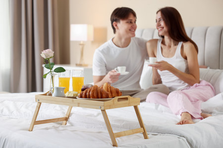 Tray with delicious breakfast and happy couple having coffee in bed, selective focus. Hotel room serviceの写真素材