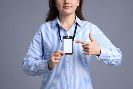 Woman pointing at her blank badge on gray background, closeupの写真素材