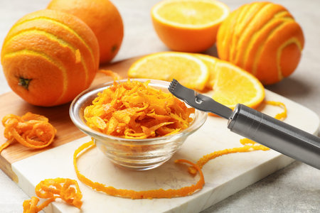Orange zest, fresh fruits and zester tool on light gray table, closeup