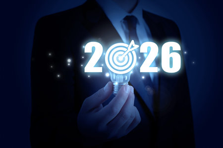 Businessman holding light bulb on dark blue background, closeup. 2026 numbers with target instead of...
