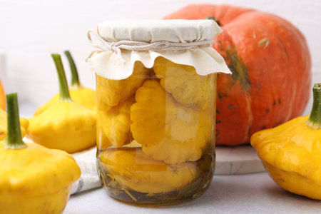 Pickled pattypan squashes in jar and fresh vegetables on light table, closeupの写真素材