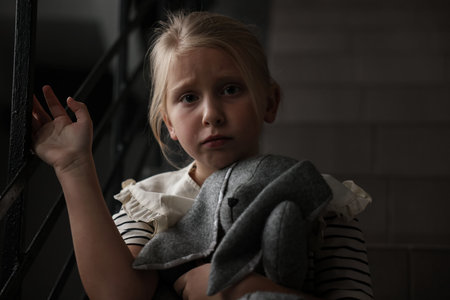 Sad little girl with toy bunny on stairs indoorsの写真素材