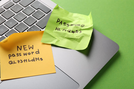 Changing password. Notes with new and old passwords and laptop on green background, closeup