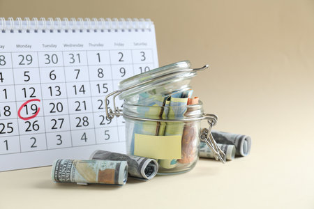 Saving money. Jar with banknotes and calendar on beige backgroundの写真素材