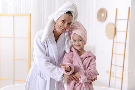 Mother and daughter wearing bathrobes with their hair wrapped in towels at bathroomの写真素材